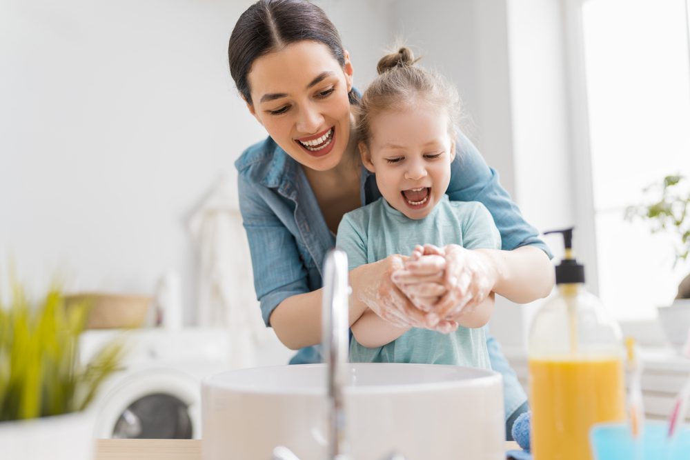 Mother helping her daughter wash her hands